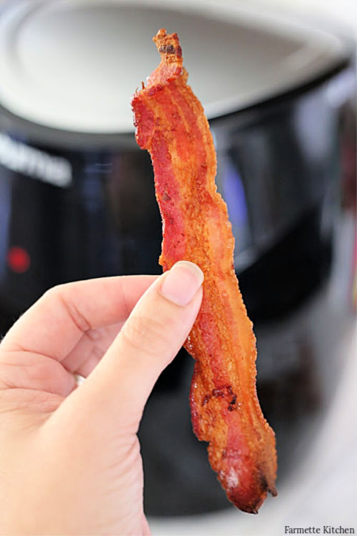 holding up a piece of cooked bacon