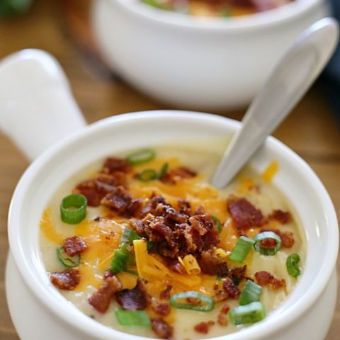 white crock filled with potato soup and toppings with a spoon