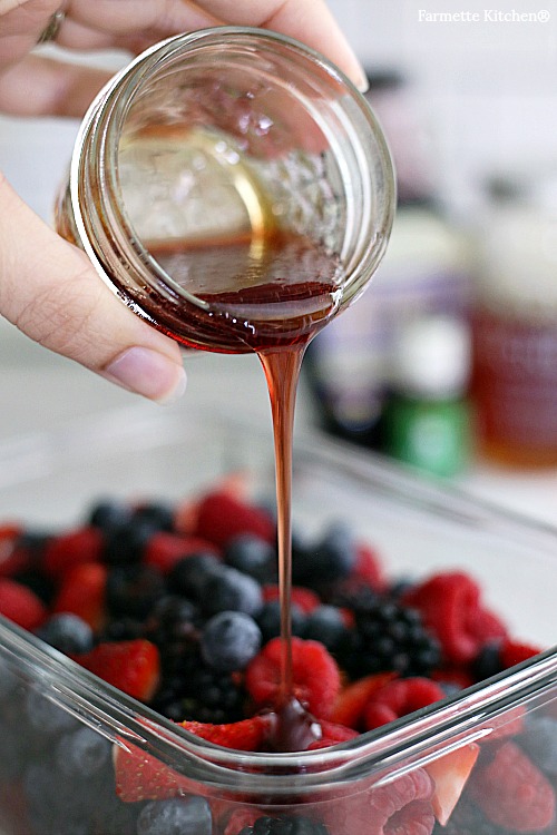 pouring Ningxia Berry Syrup and honey lime dressing over fresh fruit salad with berries