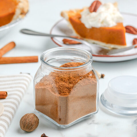 pumpkin pie spices in a jar with cinnamon sticks and whole cloves scattered around