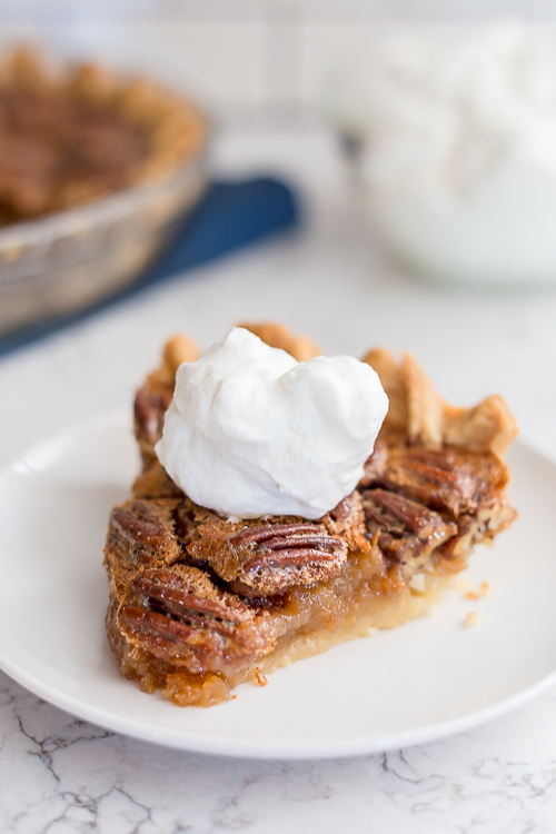 slice of pecan pie on a white plate with a big dollop of whipped cream