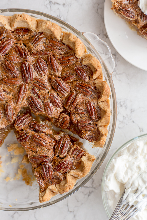 a pecan pie that has been cut into next to a bowl of whipped cream