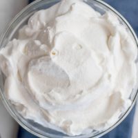glass bowl full of whipped cream next to a whisk and red strawberries