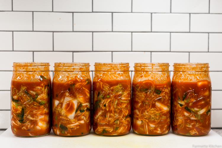 jars of kimchi lined up against a tile wall