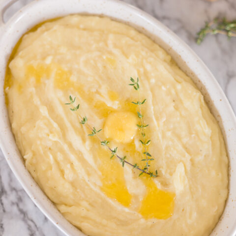 oval bowl filled with mashed potatoes and topped with butter and thyme