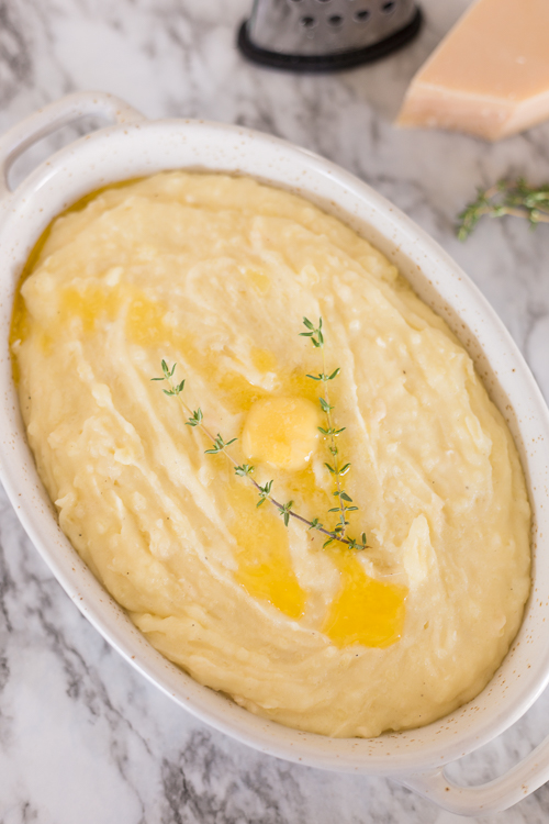 oval bowl filled with mashed potatoes and topped with butter and thyme