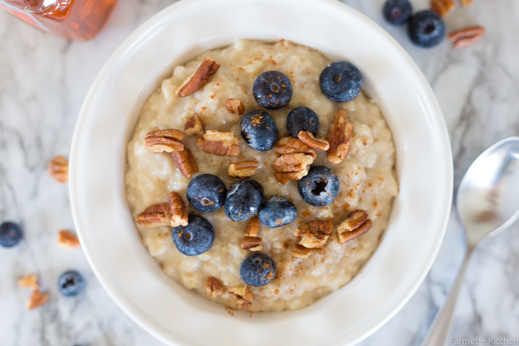 white bowl with oatmeal topped with pecans and blueberries