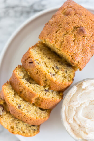 a loaf of pumpkin banana bread sliced next to a bowl of butter