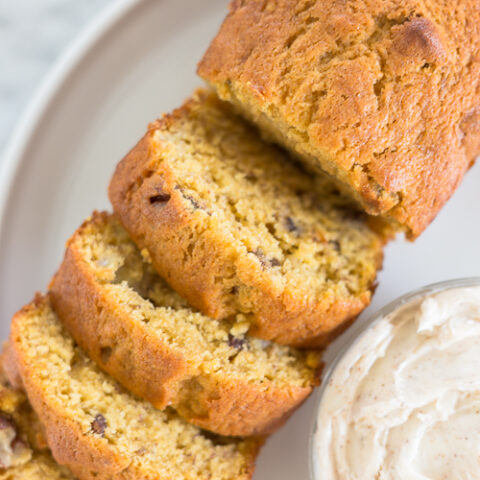 a loaf of pumpkin banana bread sliced next to a bowl of butter