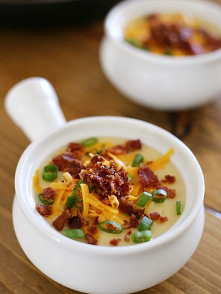 crock with potato soup topped with cheese, bacon, and onions