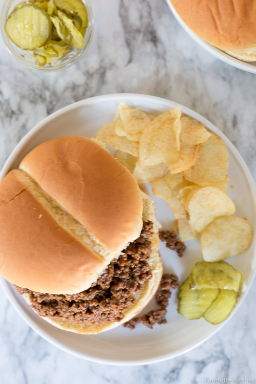 sloppy joe on a plate with chips and pickles