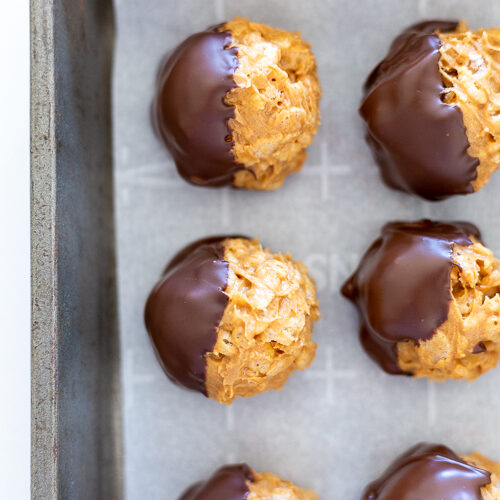 Peanut butter balls with rice krispies dipped in chocolate on a baking sheet