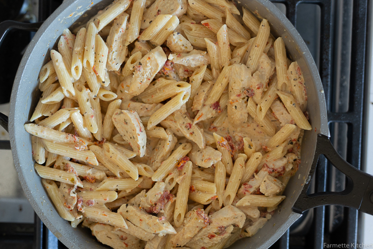 penne pasta tossed with cream sauce and sliced chicken in a skillet