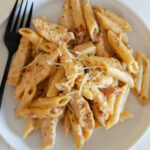 creamy tuscan chicken pasta with a black fork on a white plate